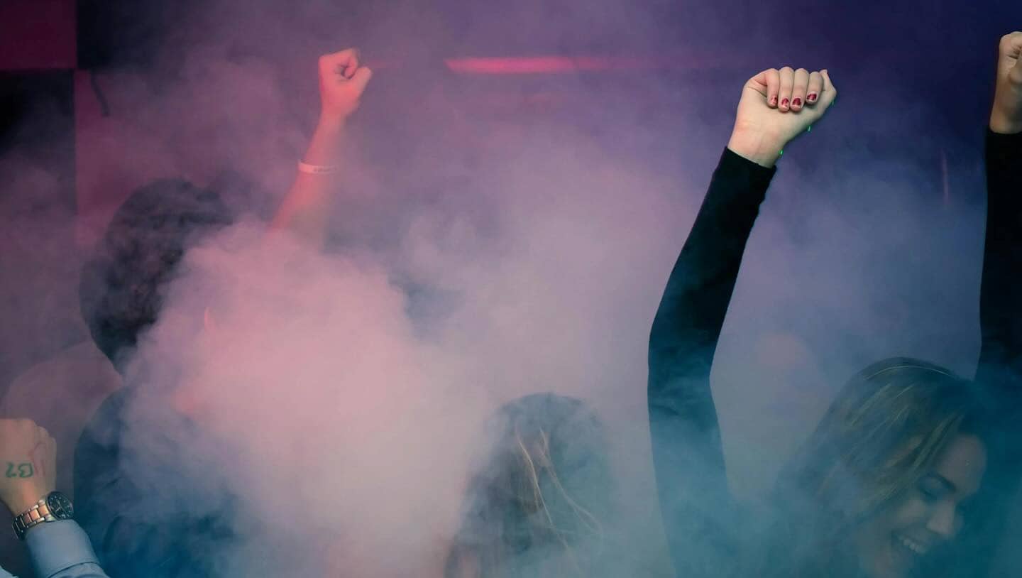 Handen in de lucht op een clubfeest, in rook en gekleurd licht