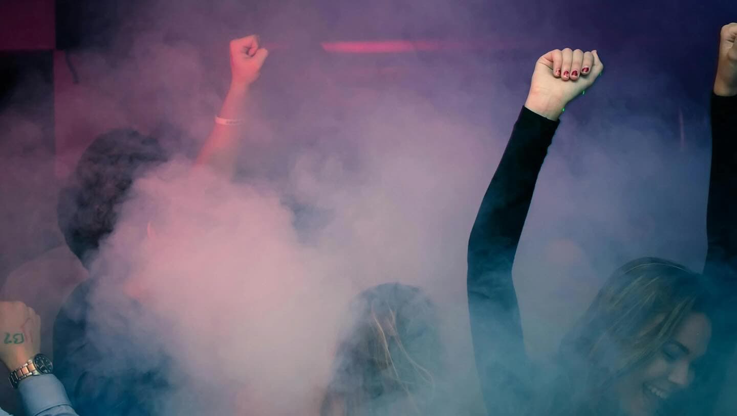 Handen in de lucht op een clubfeest, in rook en gekleurd licht